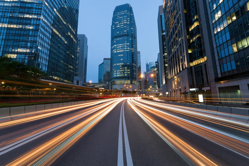 Light trails from moving vehicles on a city highway at dusk surrounded by skyscrapers