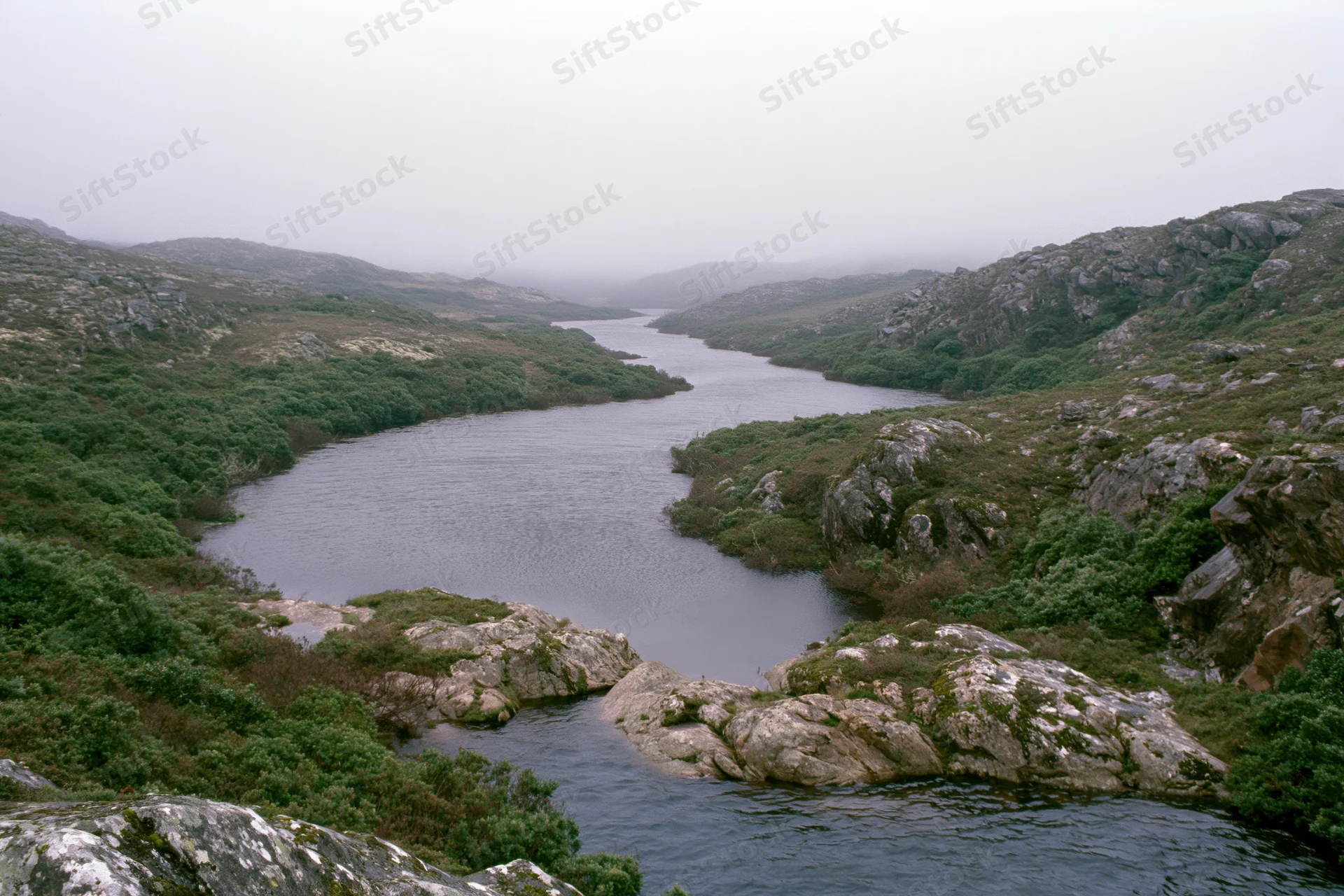 Misty river winding through rocky hills covered in green vegetation and mossy stones