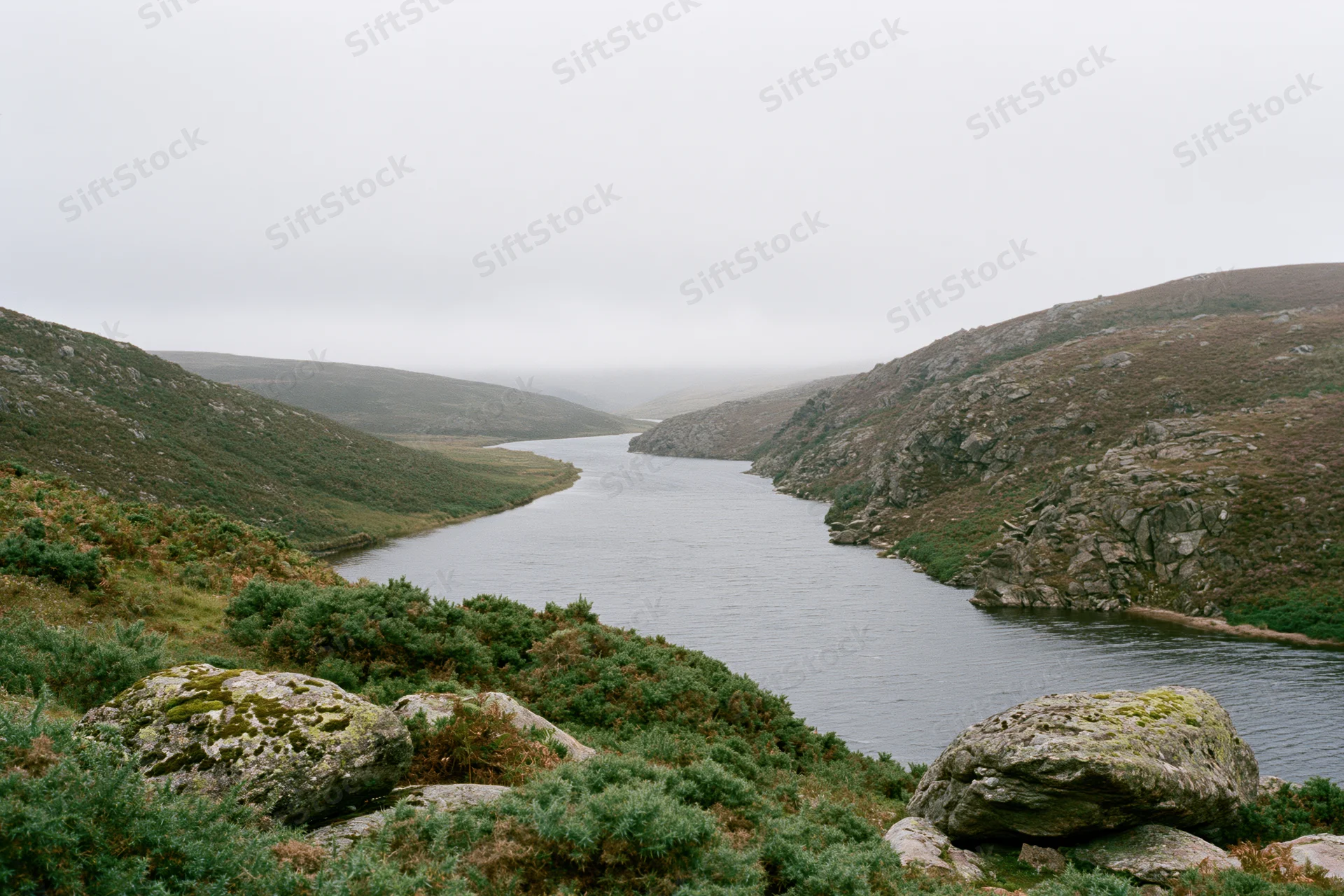 Misty river winding through low rocky hills covered in green vegetation and mossy stones