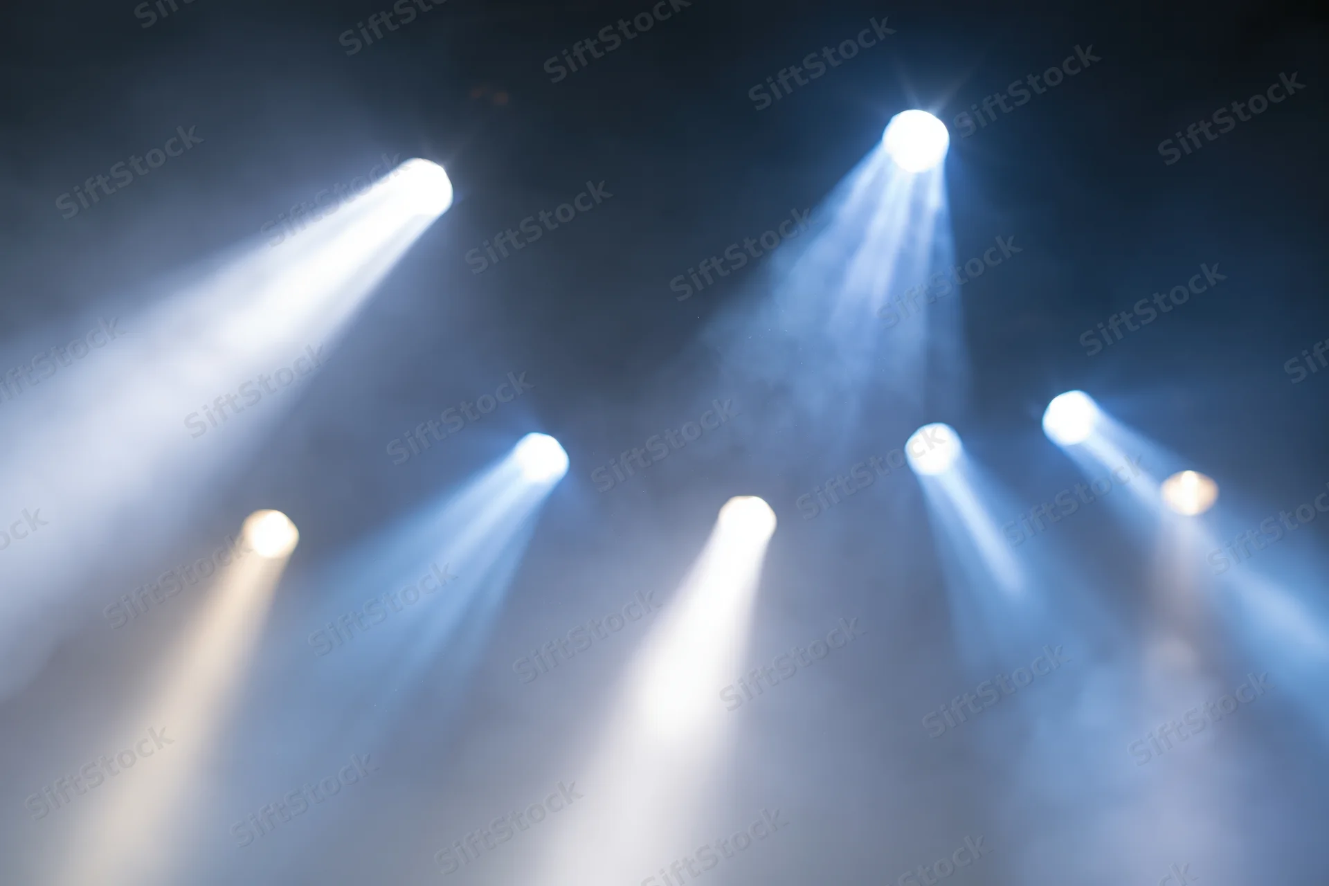 Multiple spotlights casting beams through haze in a dark stage environment