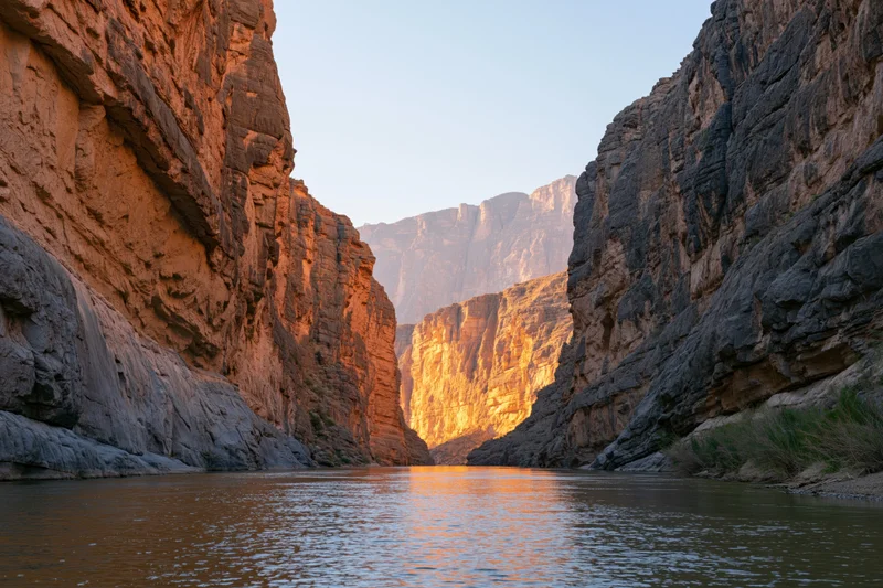 Narrow desert canyon with towering sandstone walls flanking a calm river at sunset