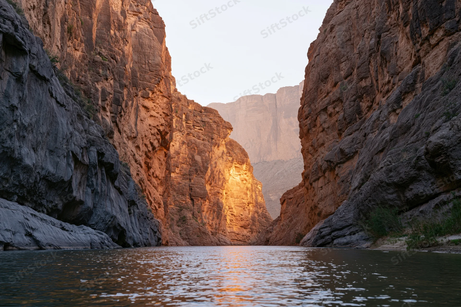 Narrow desert canyon with towering sandstone walls flanking a calm river at golden hour