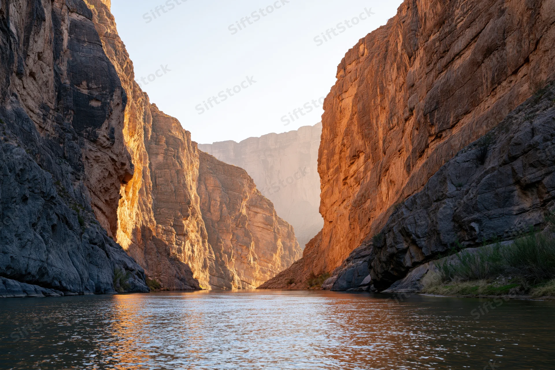 River flowing through narrow desert canyon flanked by towering sandstone cliffs at golden hour