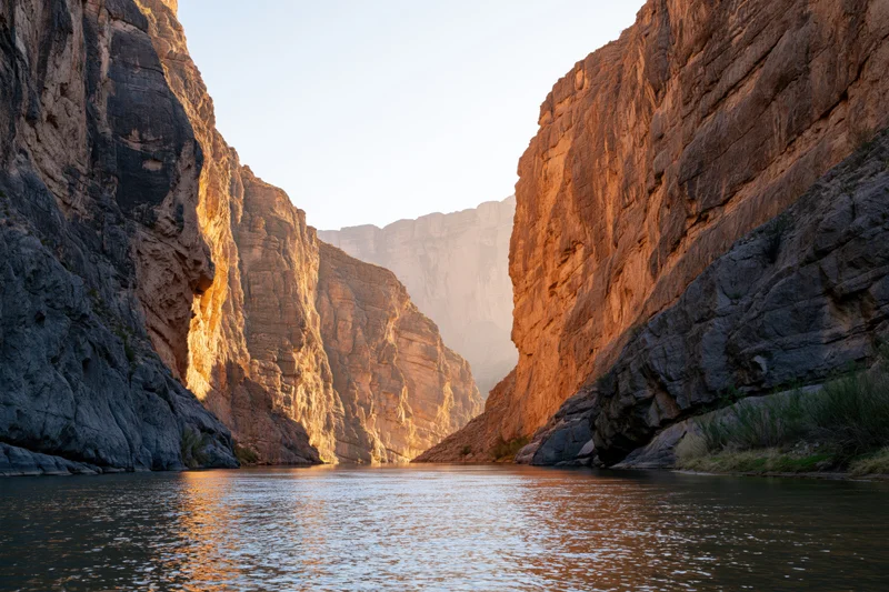 River flowing through narrow desert canyon flanked by towering sandstone cliffs at golden hour