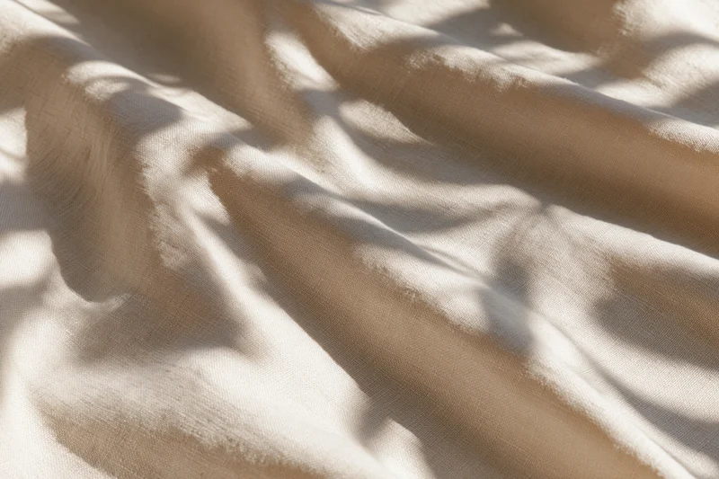 Natural linen fabric with soft diagonal folds and dappled shadows laid flat