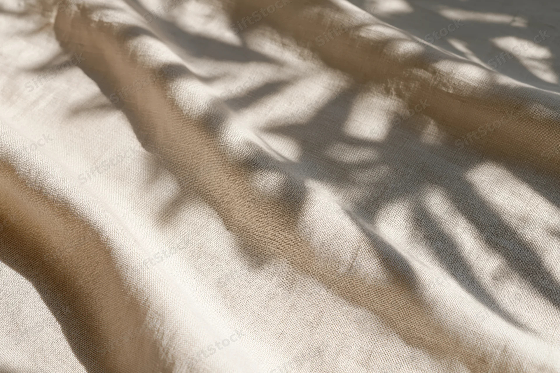 Natural linen fabric with soft diagonal folds and dappled leaf shadows cast across its surface
