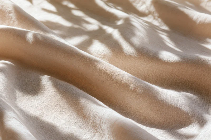 Natural linen fabric with soft diagonal folds and dappled sunlight shadows