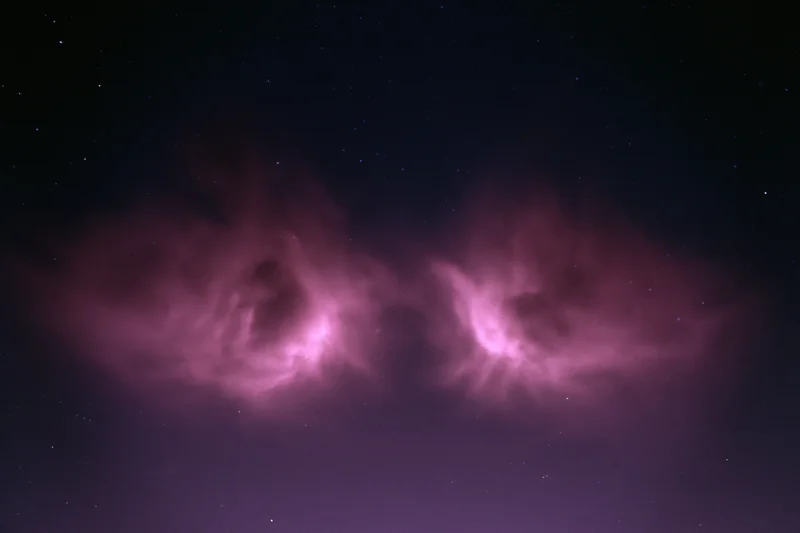 Two glowing magenta-pink nebulae in the night sky