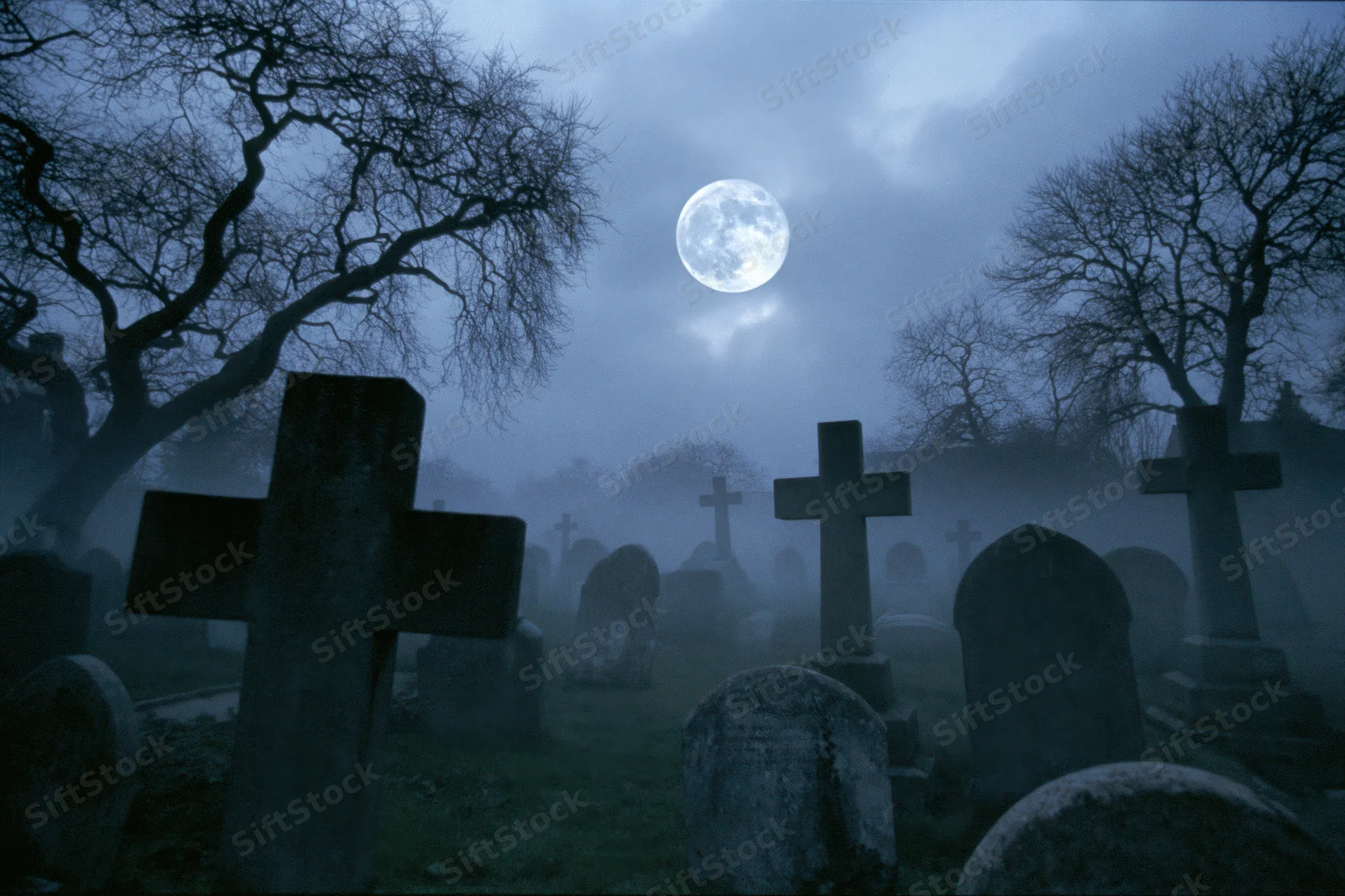 Old graveyard with weathered stone crosses and tombs under a full moon at night in fog