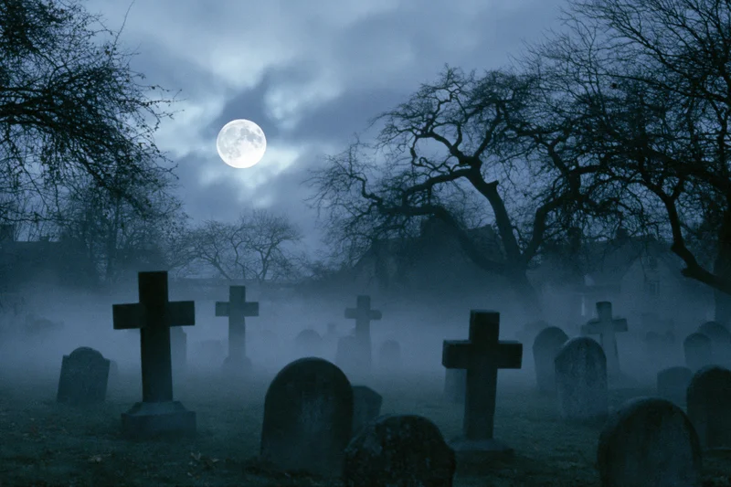 Old graveyard with weathered stone crosses and tombs under a full moon at night in fog