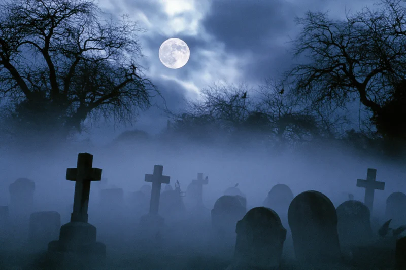 Old graveyard with weathered stone crosses and tombs under a full moon at night in fog