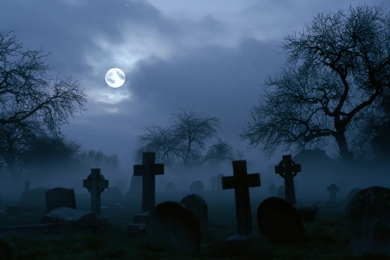 Old graveyard with weathered stone crosses and tombs under a full moon at night in fog