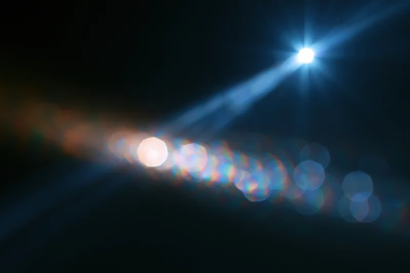 Bright lens flare with blue starburst and rainbow bokeh on dark background