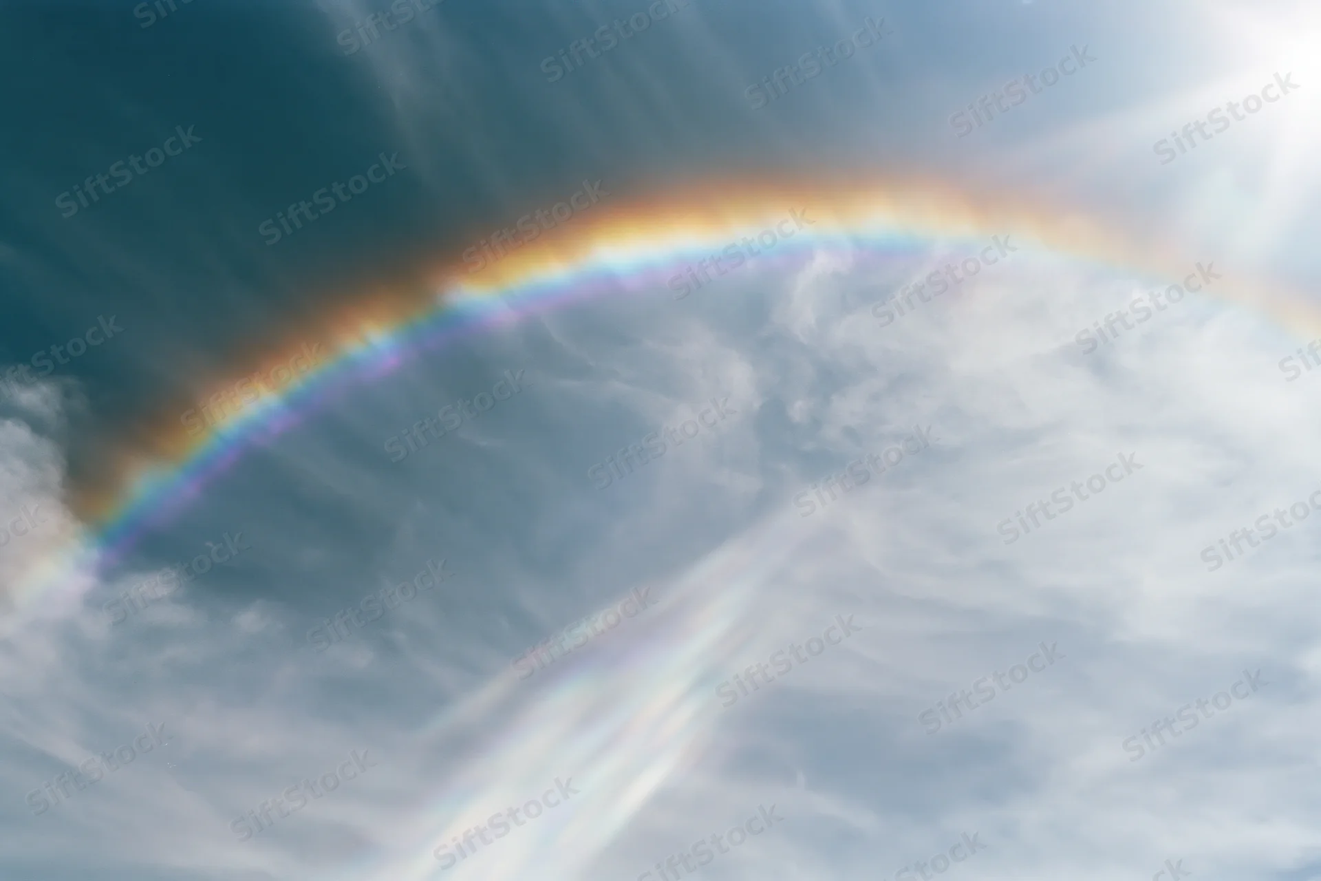 Rainbow arching across overexposed sky with wispy clouds viewed from below