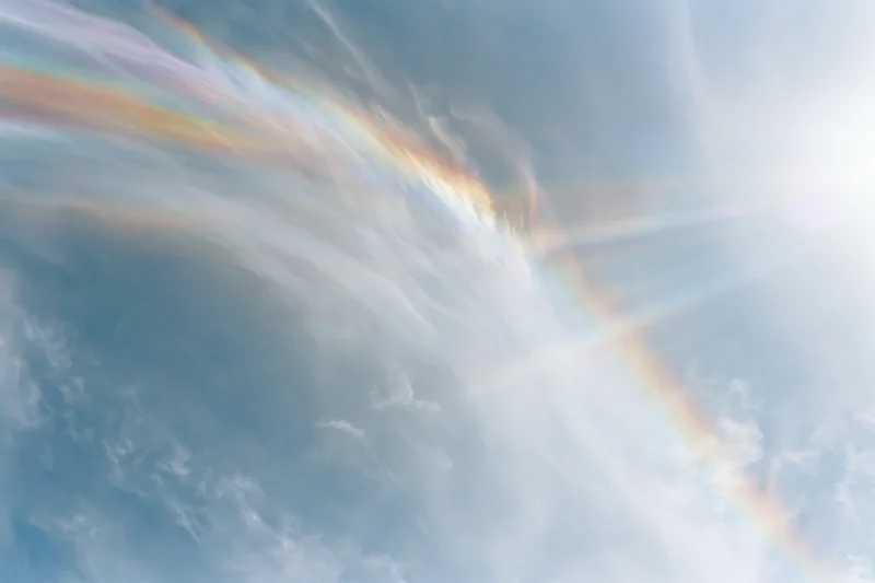 Overexposed daytime sky with wispy clouds and a rainbow halo effect viewed directly upward