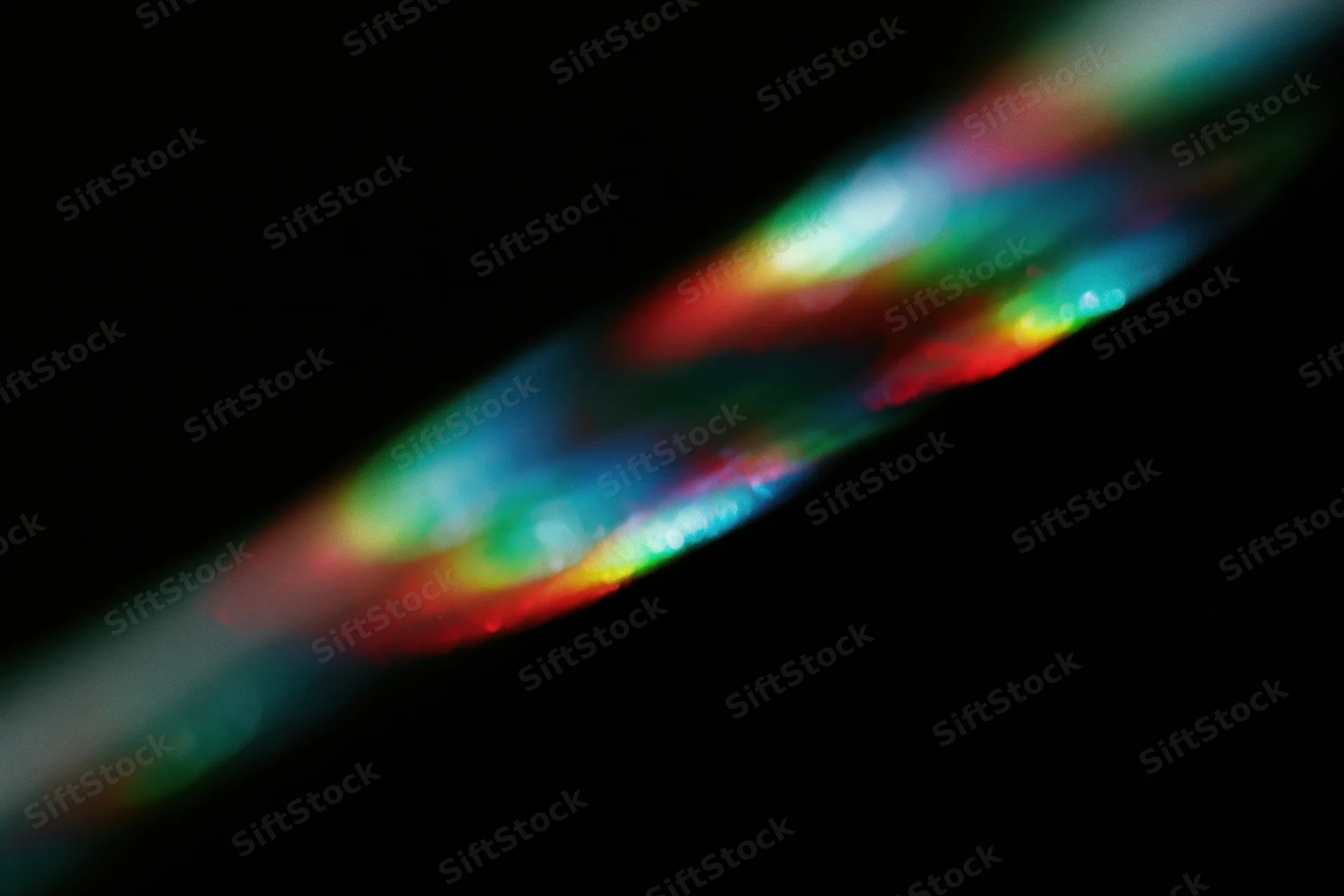 Prismatic light scattering across a black background in a diagonal band of rainbow colors