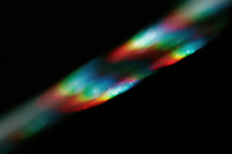 Prismatic light scattering across a black background in a diagonal band of rainbow colors