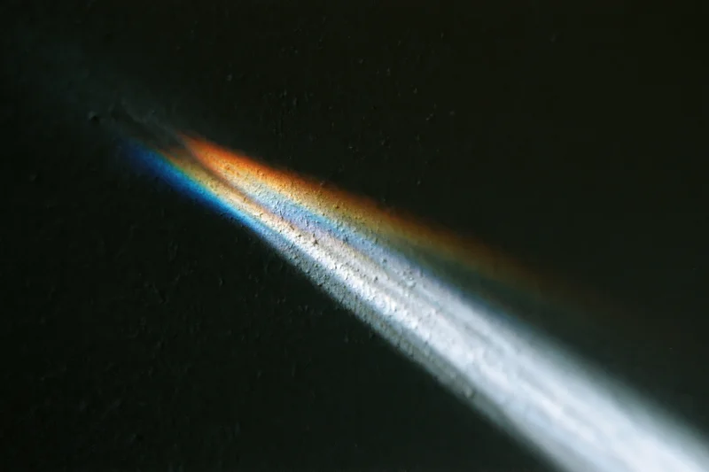 Prismatic light beam casting rainbow spectrum on dark surface