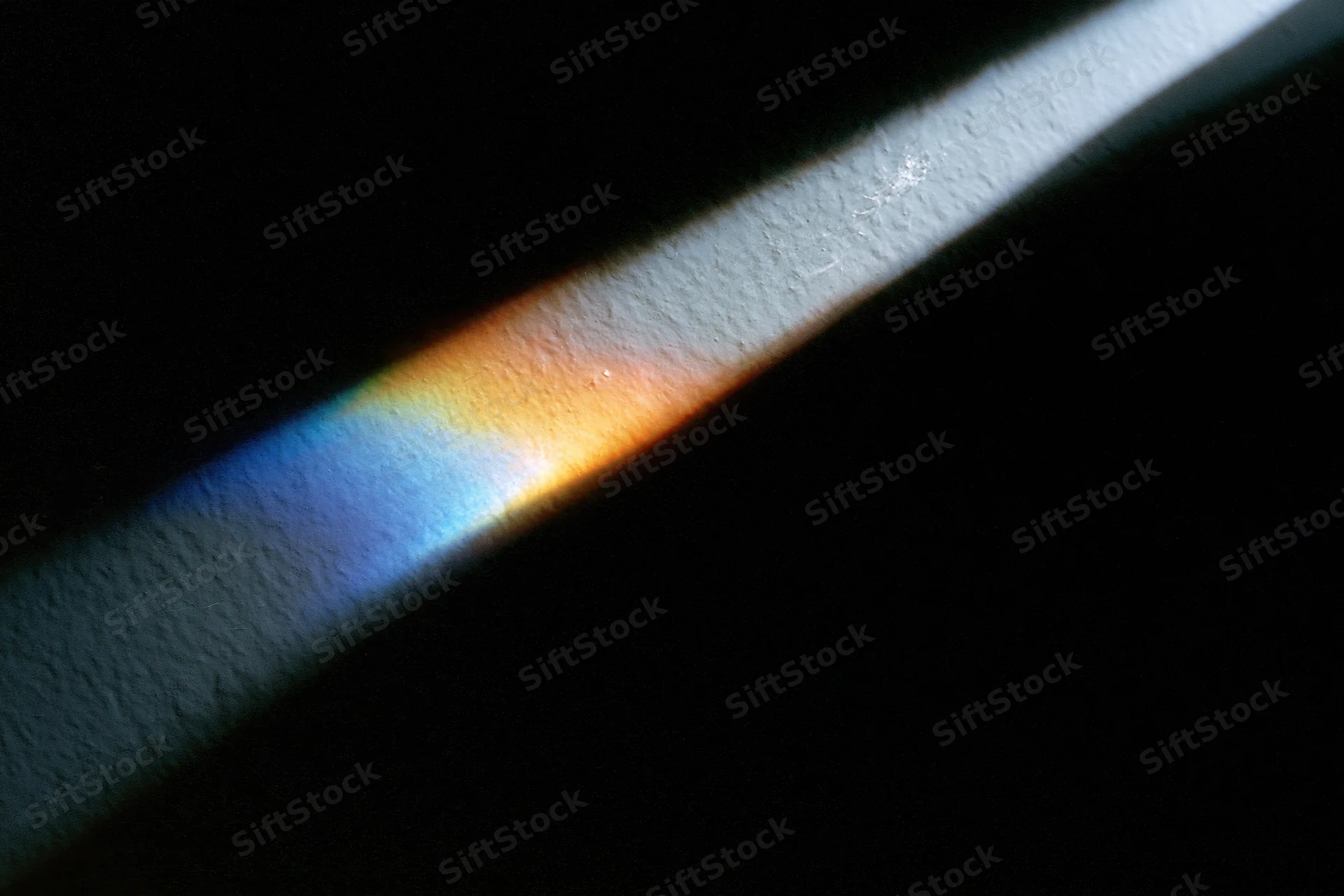 Prismatic light refraction casting rainbow spectrum on textured white surface
