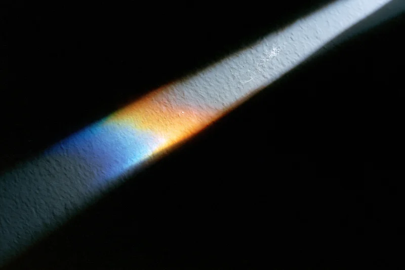 Prismatic light refraction casting rainbow spectrum on textured white surface