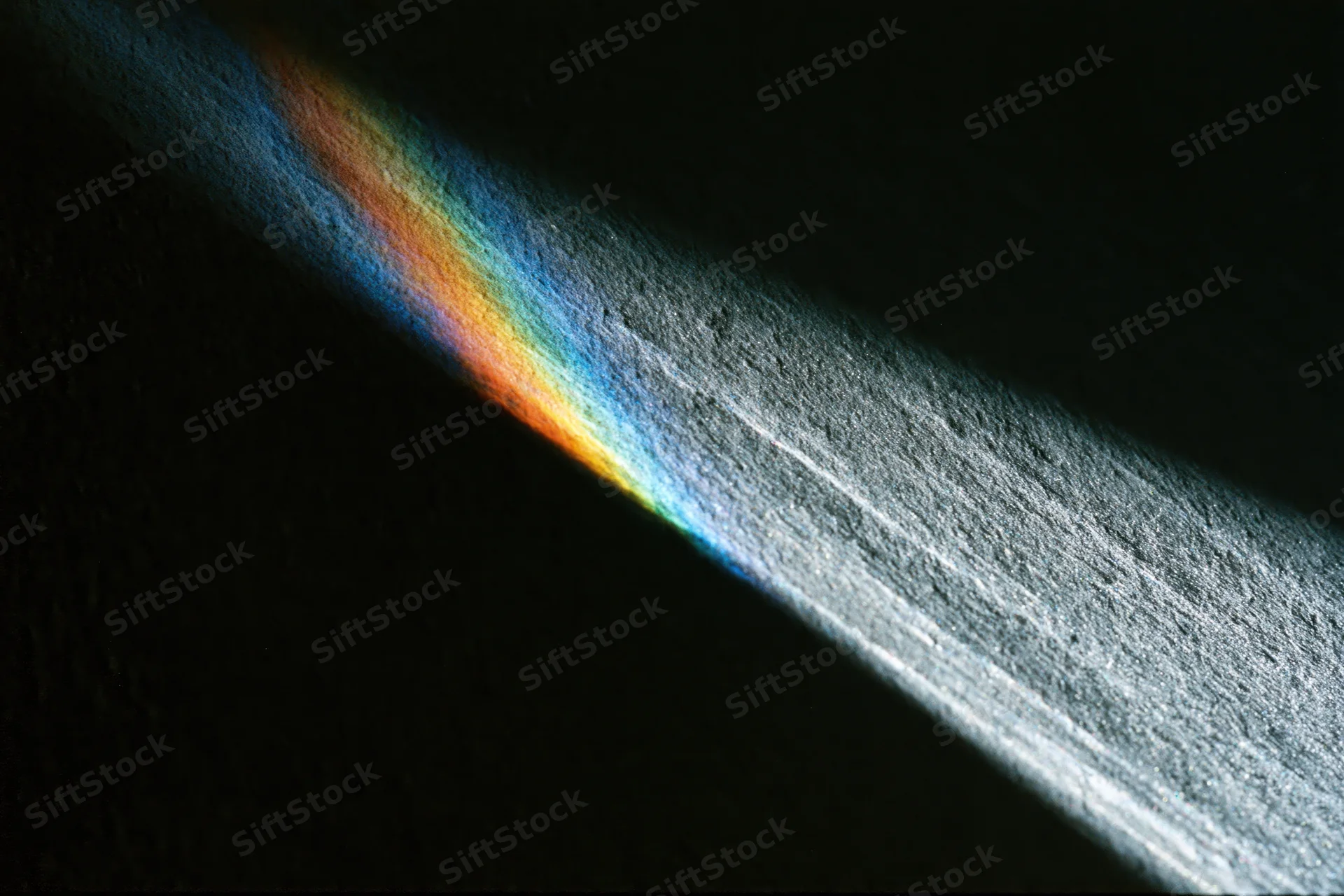 Prismatic light refraction casting rainbow spectrum and white beam on dark textured surface