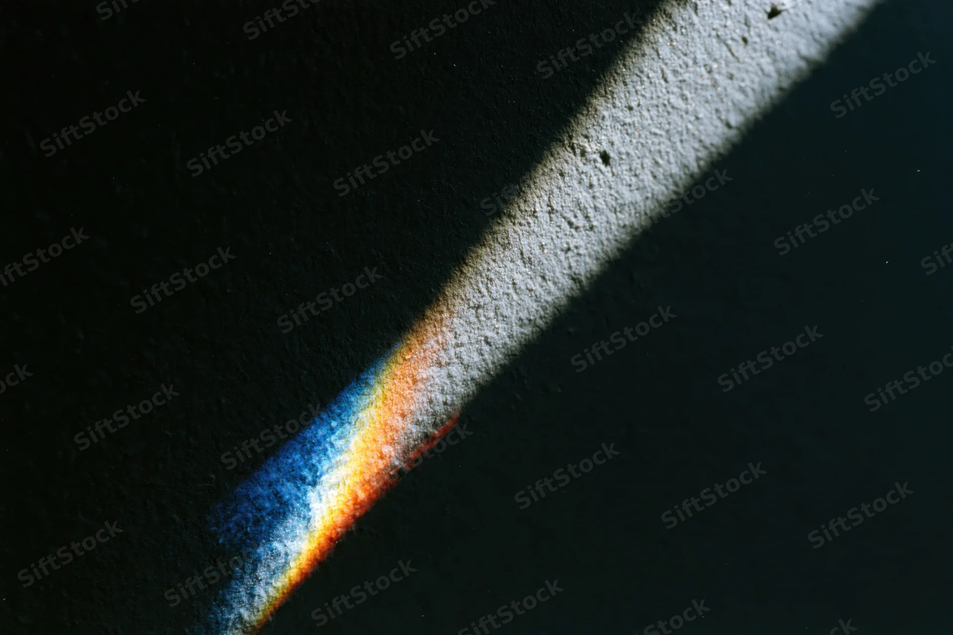 Prismatic light refraction casting rainbow spectrum on dark textured surface with white highlight and shadow