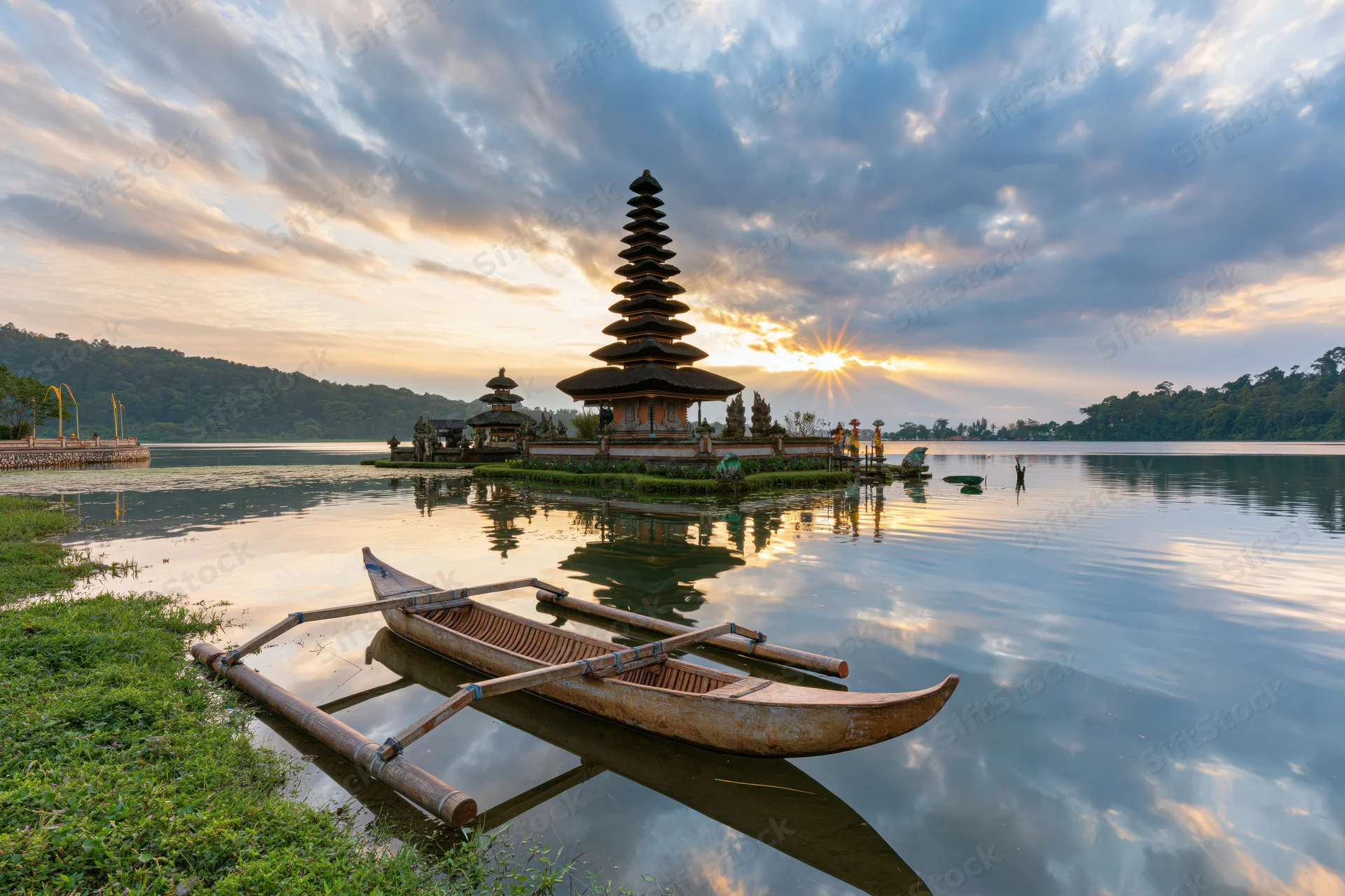 Balinese water temple rising from calm lake at sunrise with outrigger boat in foreground
