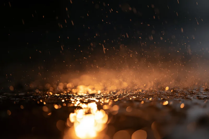 Rain falling on a wet dark surface at night with golden light reflections and bokeh effects