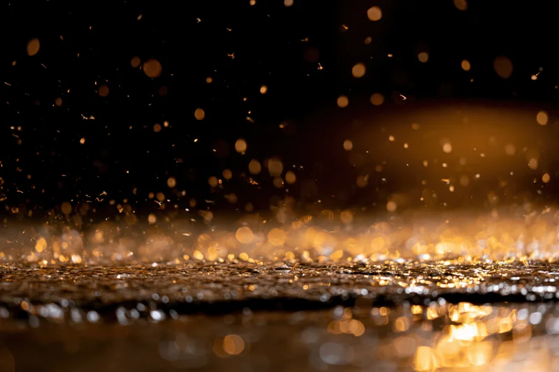 Rain falling on a wet dark surface at night creating golden reflections and bokeh lights