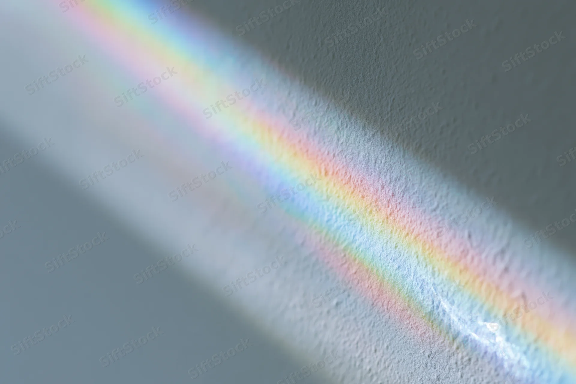 Rainbow light refraction cast across a pale gray-white wall surface