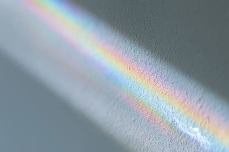 Rainbow light refraction cast across a pale gray-white wall surface