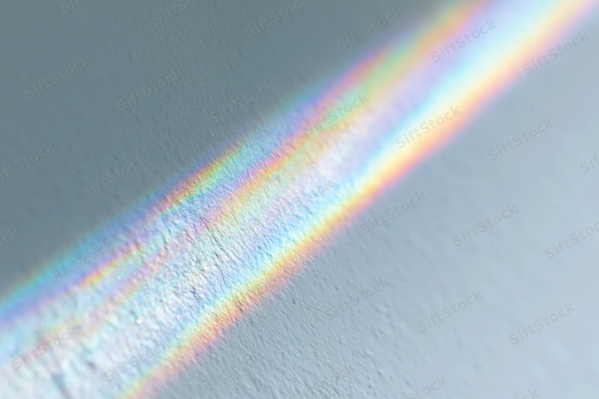 Rainbow light refraction cast across a pale gray-white textured wall interior