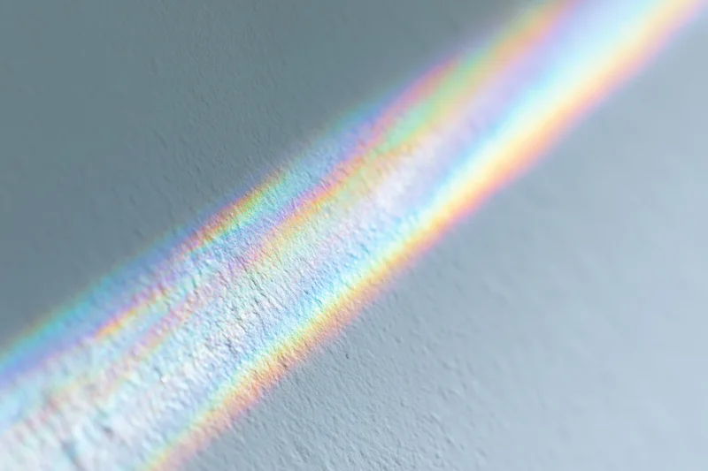Rainbow light refraction cast across a pale gray-white textured wall interior