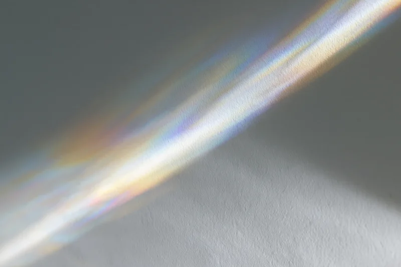 Rainbow light refraction casting diagonal prismatic spectrum across gray wall surface