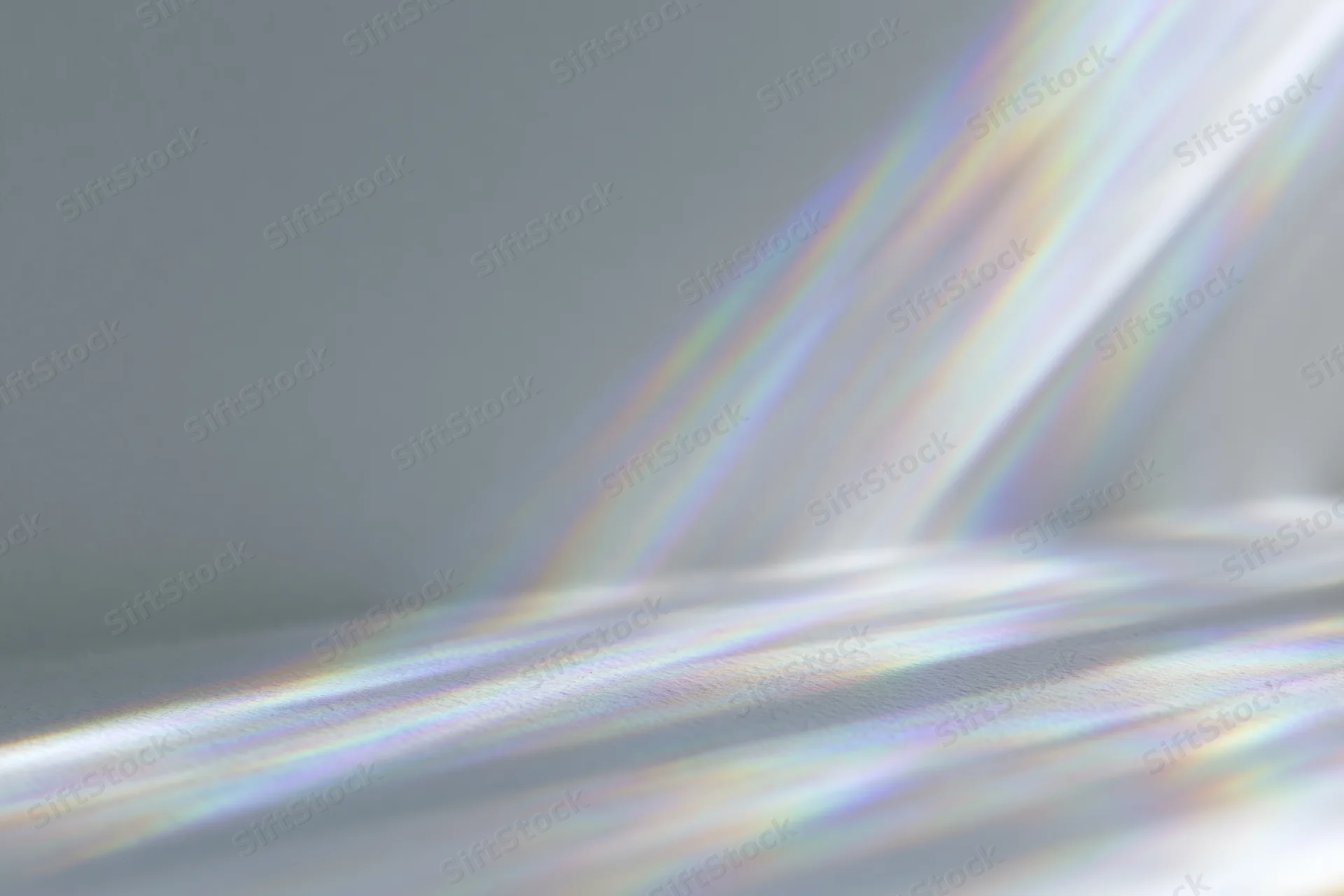 Rainbow light refraction rays casting prismatic lens flares across a smooth gray surface in a studio setting