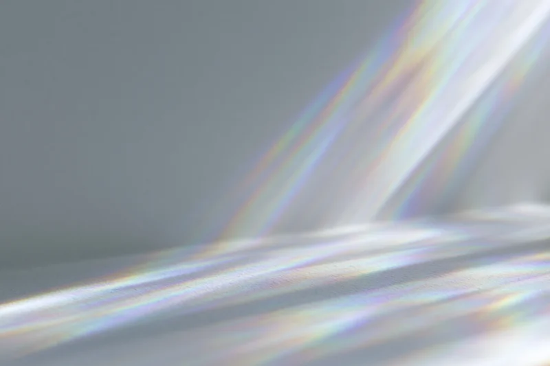 Rainbow light refraction rays casting prismatic lens flares across a smooth gray surface in a studio setting
