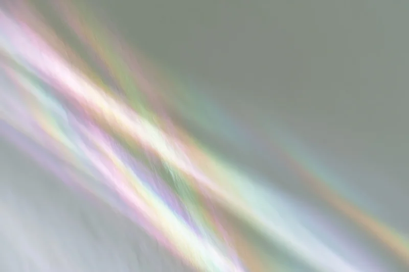 Rainbow light refraction streaks falling diagonally across a pale white background