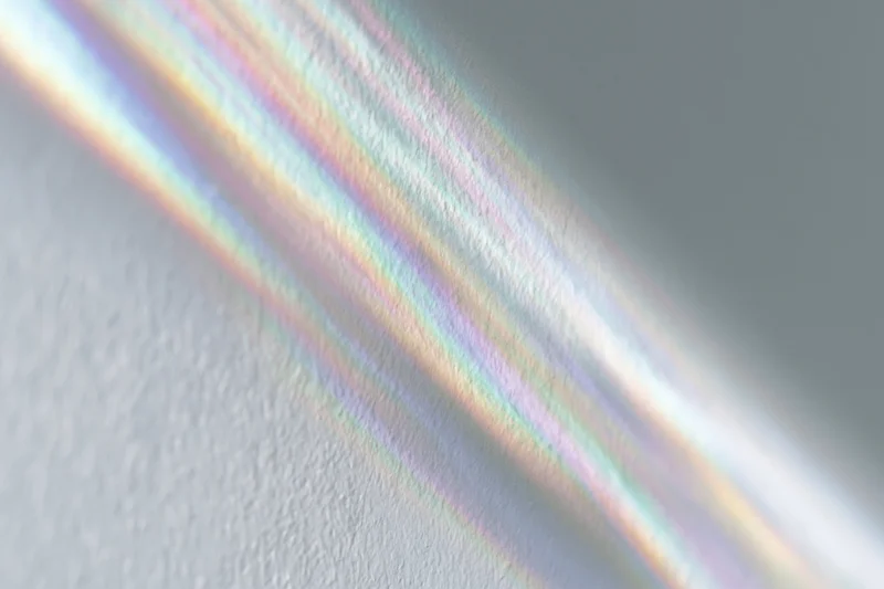 Rainbow light refraction streaks falling across a pale white wall