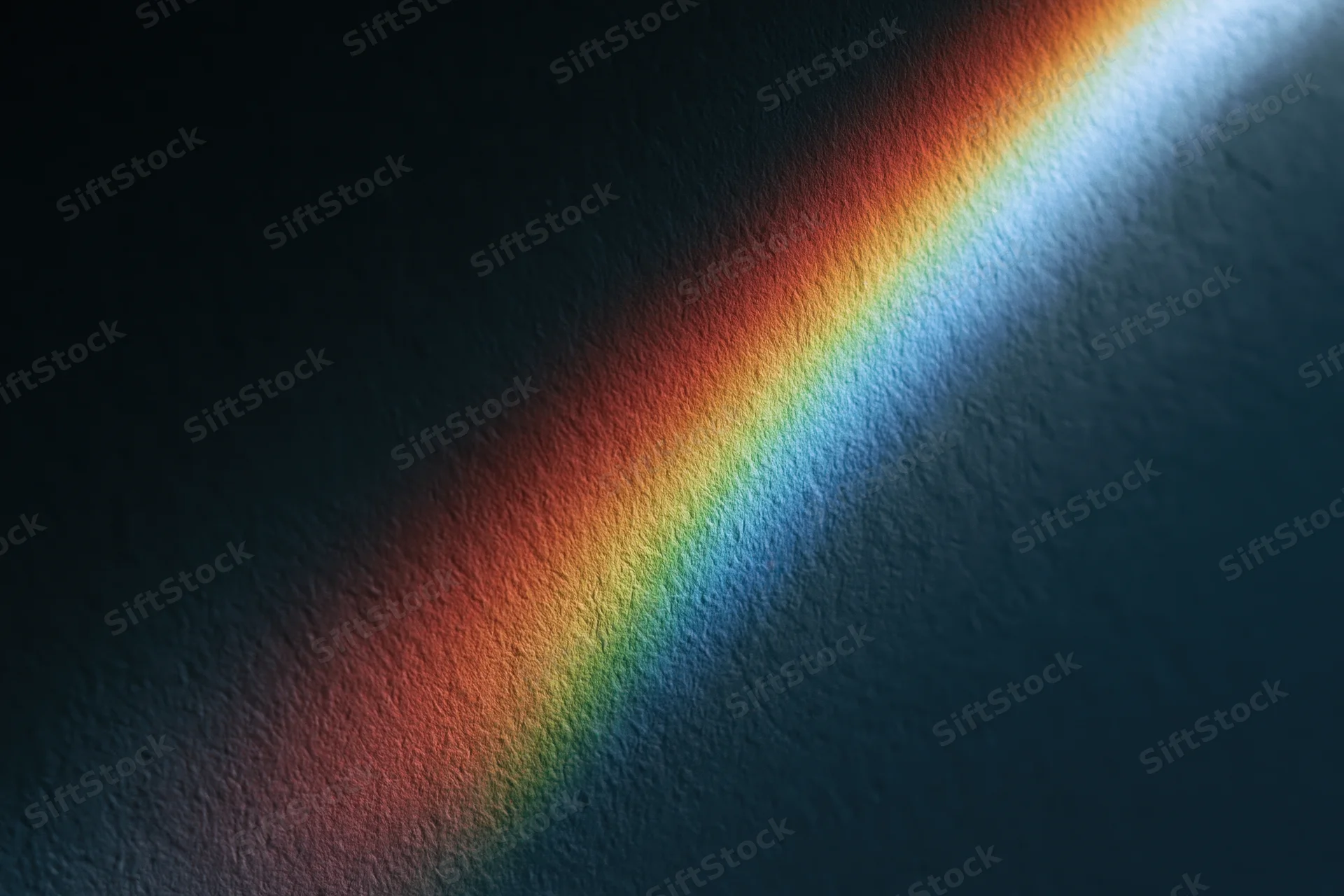 Rainbow spectrum light projection cast diagonally across a textured dark wall