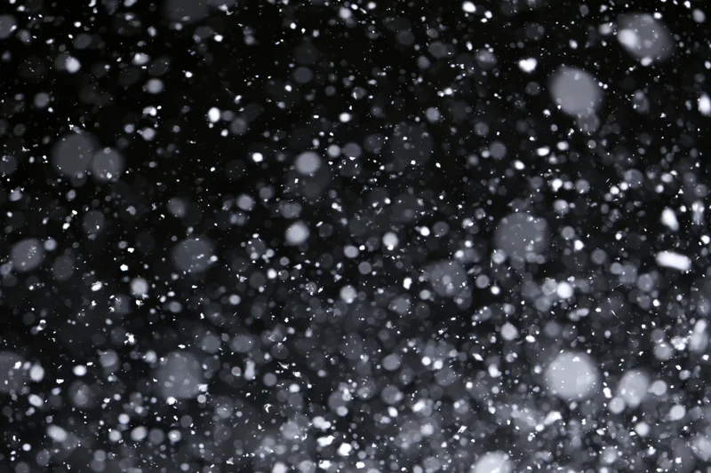 Snowflakes falling densely against a black night sky