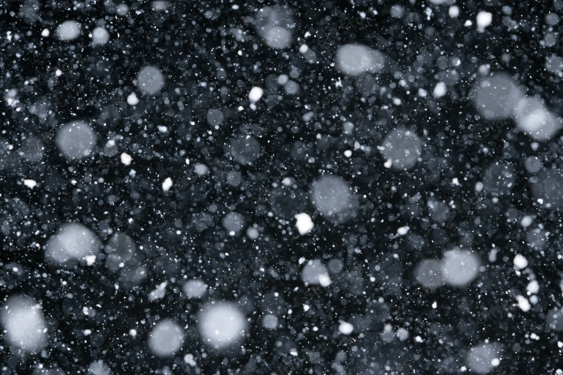 Snowflakes falling densely against a black night sky
