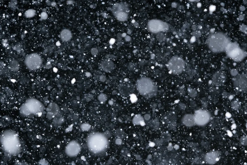 Snowflakes falling densely against a black night sky