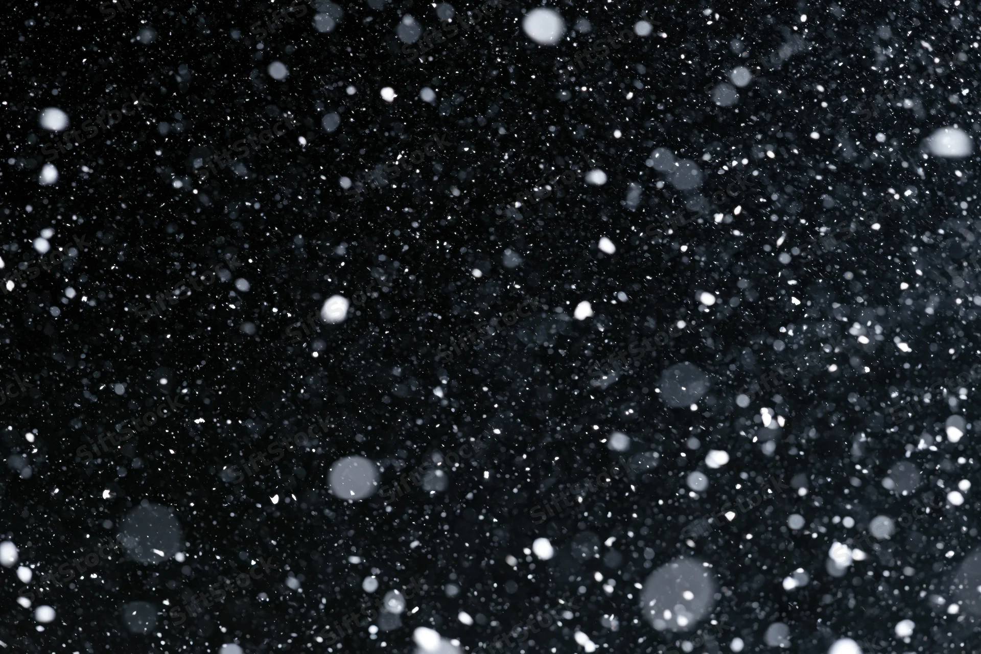 Snowflakes falling densely against a black night sky