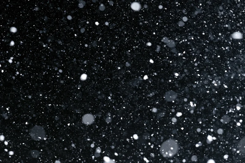 Snowflakes falling densely against a black night sky