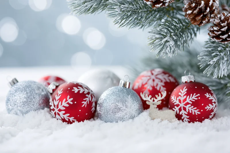 Red and silver christmas ornaments with snowflake patterns arranged in snow beneath frosted pine branches