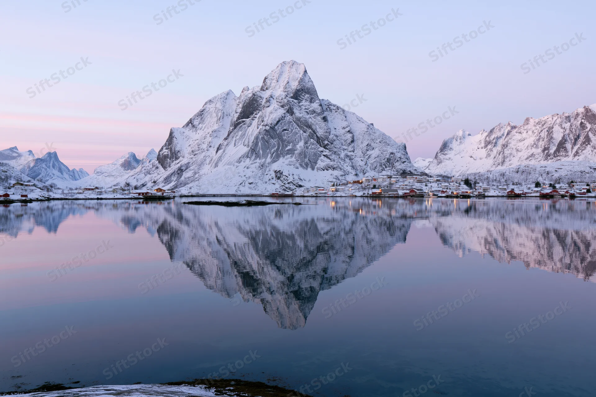 Snow-covered mountains reflected in calm water at twilight in reine fishing village, lofoten islands, norway