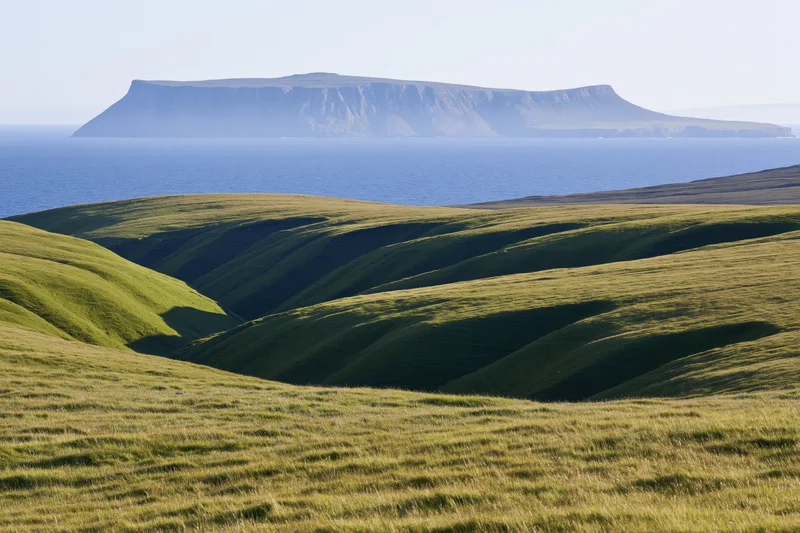 Rolling green hills with deep shadows leading to a distant island across the sea