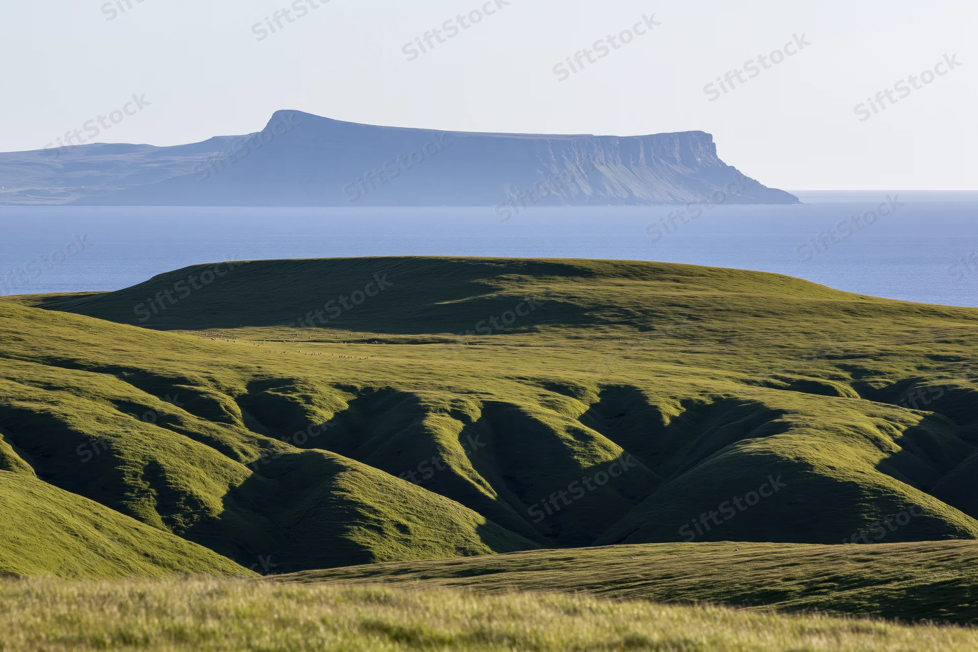Rolling green highland hills with deep shadows near the coast under a clear sky