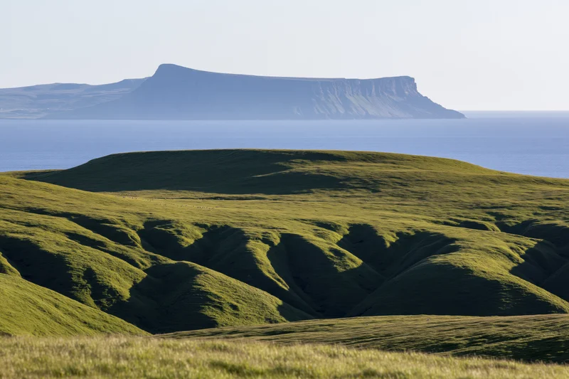 Rolling green highland hills with deep shadows near the coast under a clear sky