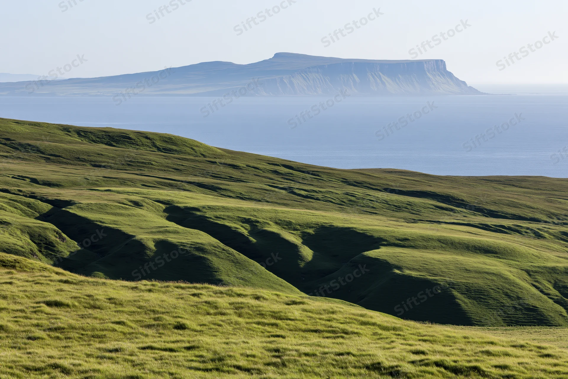 Rolling green highland hills with deep shadows overlooking the ocean and a distant cliffed island